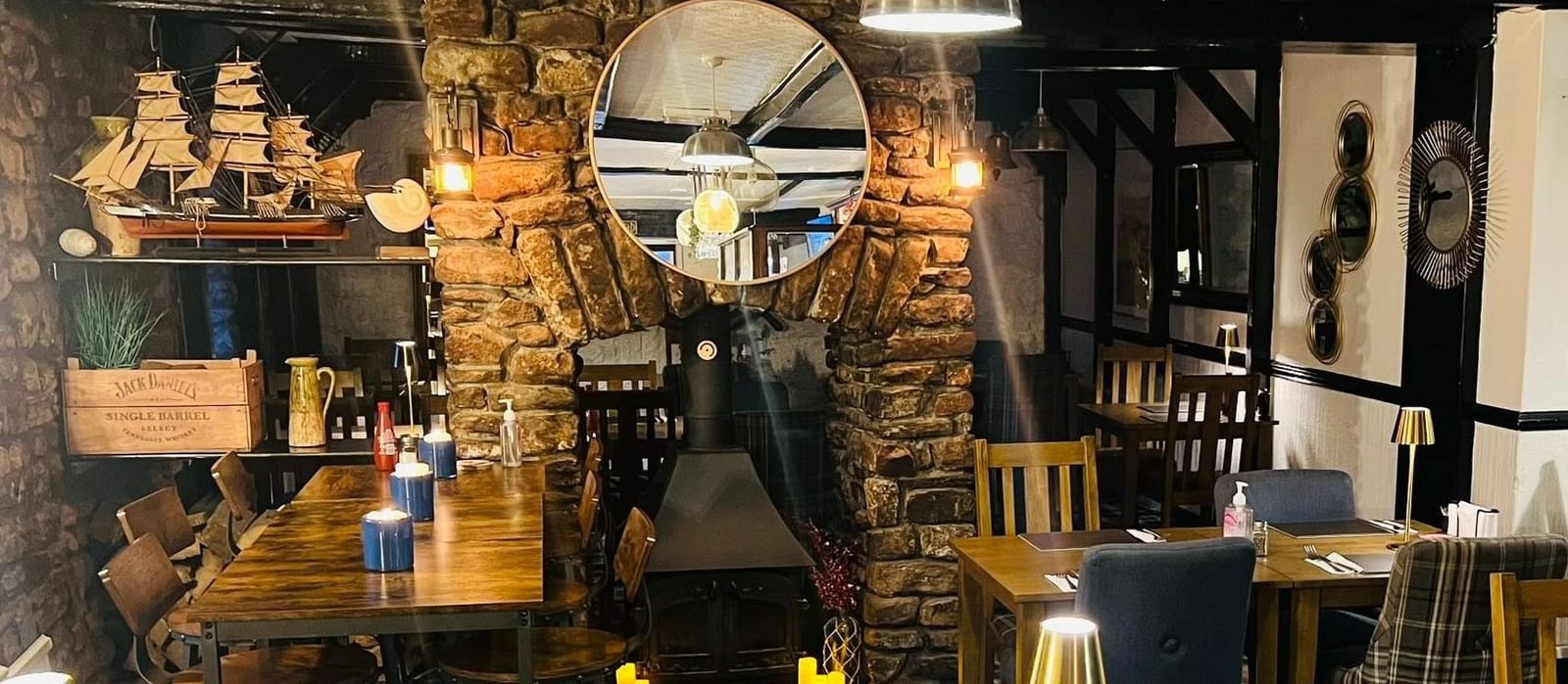 The dining room at The Ship Inn: stone walls and a stone fireplace with a round mirror, a ship model on a shelf, and set tables