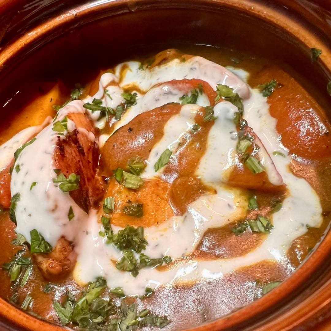 A clay pot of curry with a swirl of cream and fresh herbs