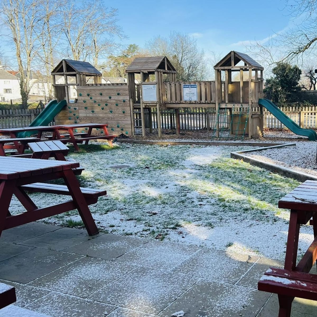 The garden and play area on a frosty morning, with red picnic benches in front of the wooden climbing frame
