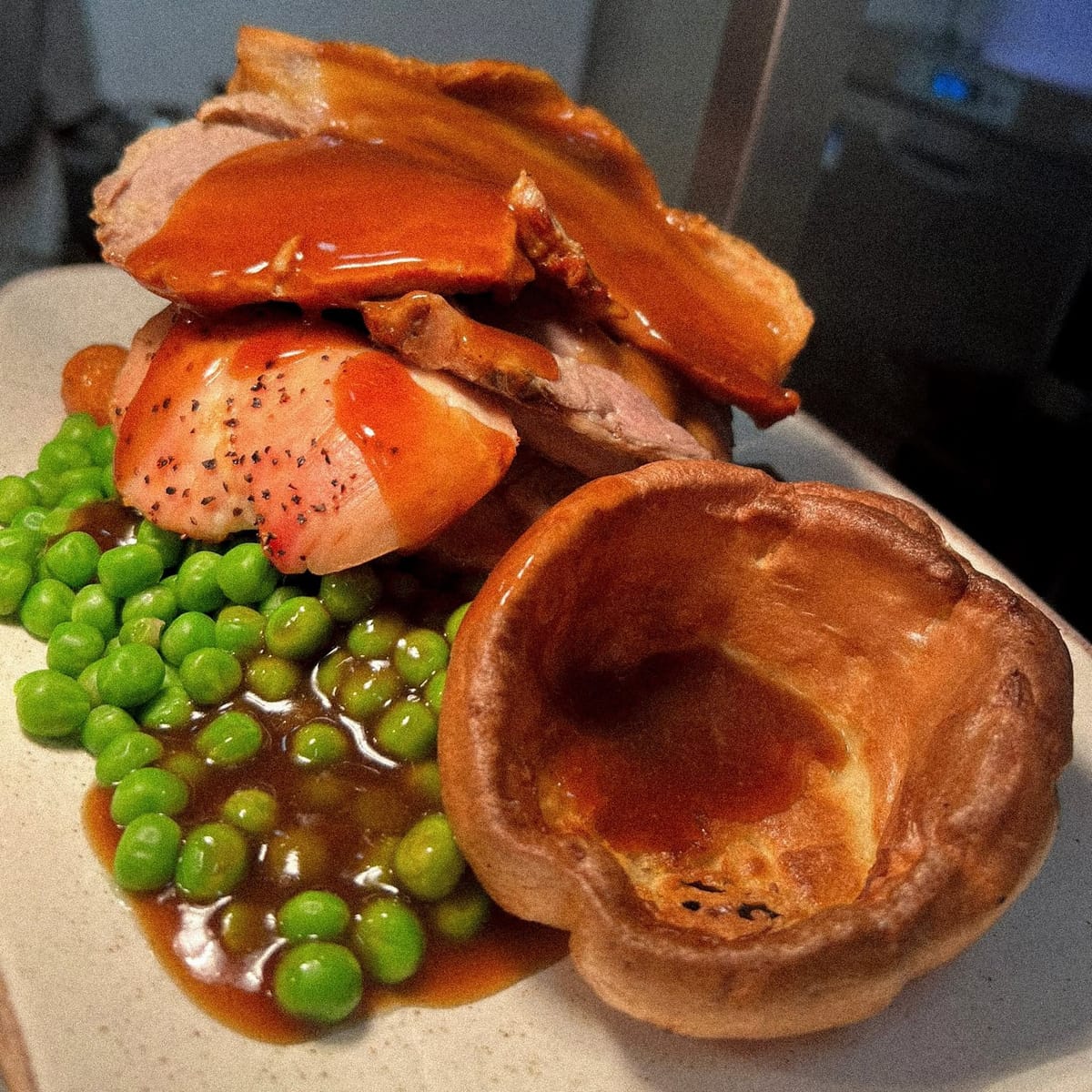 A roast dinner of sliced roast meat with a large Yorkshire pudding, peas and gravy