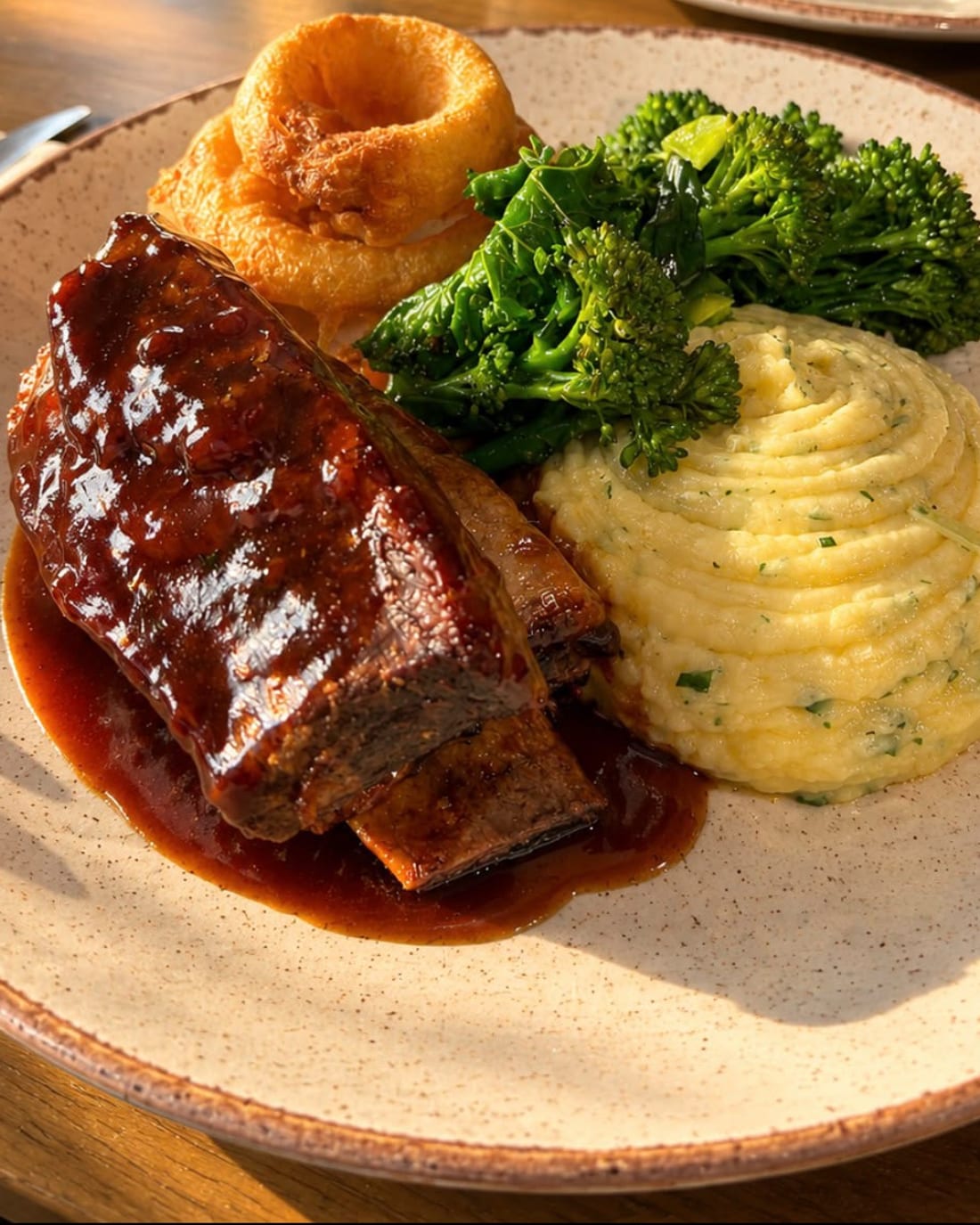 Glazed beef short rib on a plate with cheddar mash, greens, onion rings and red wine gravy