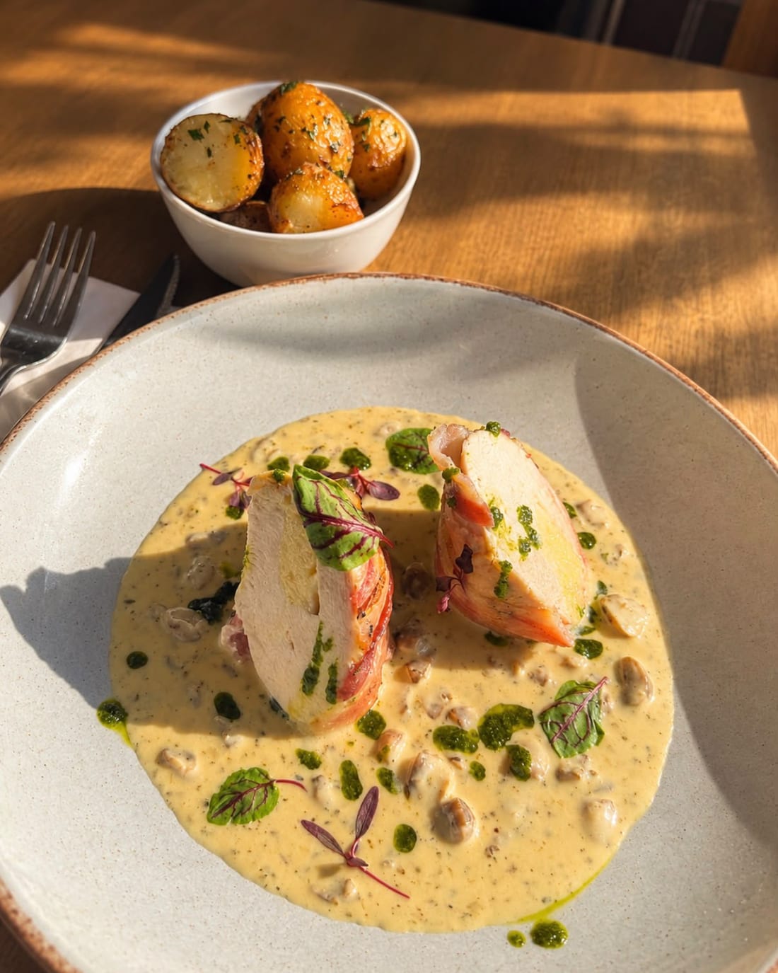 Stuffed chicken cut in two on a pool of creamy mushroom sauce in a wide bowl, with a small bowl of roasted new potatoes behind