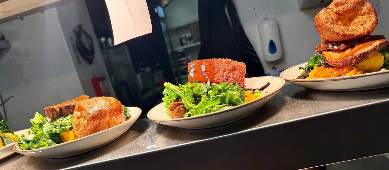 Roast dinners lined up on the kitchen pass, each with a Yorkshire pudding, greens and gravy