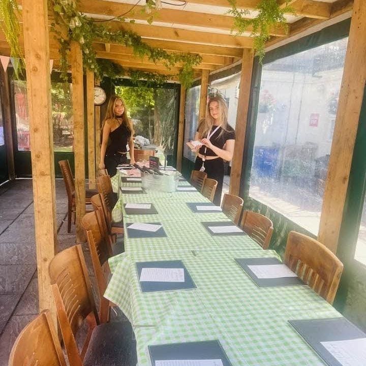 The covered garden terrace set for a group, with one long table, a green gingham cloth and menus laid out
